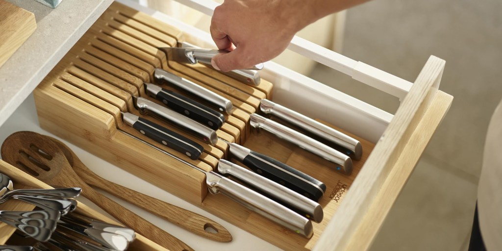 A hand holding a knife in a wooden drawer