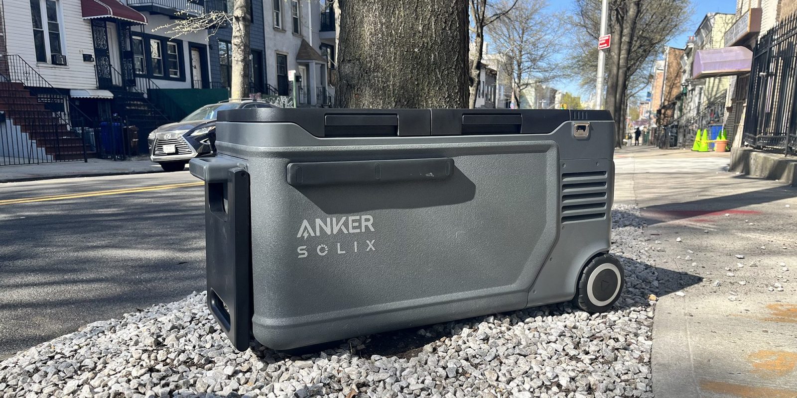 A grey cooler on gravel next to a tree