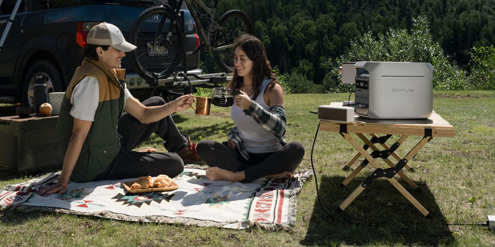A man and woman sitting on a blanket outside