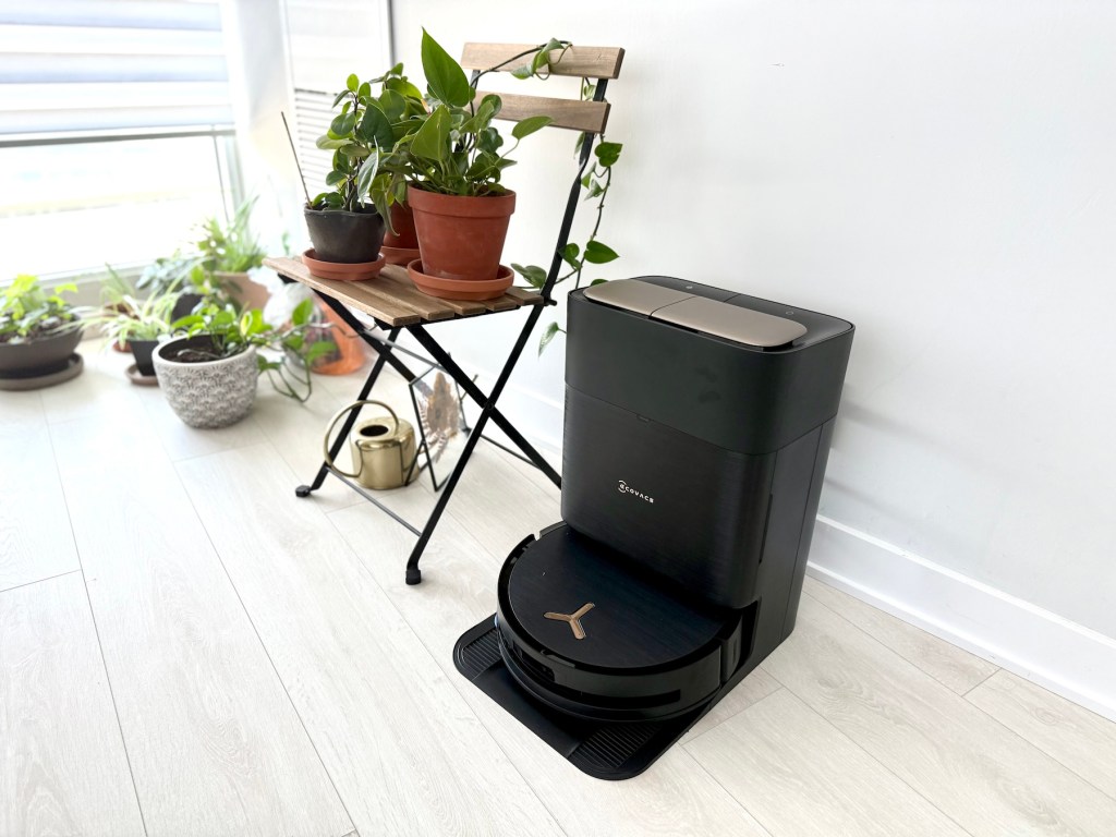 A robot vacuum cleaner next to a chair and potted plants