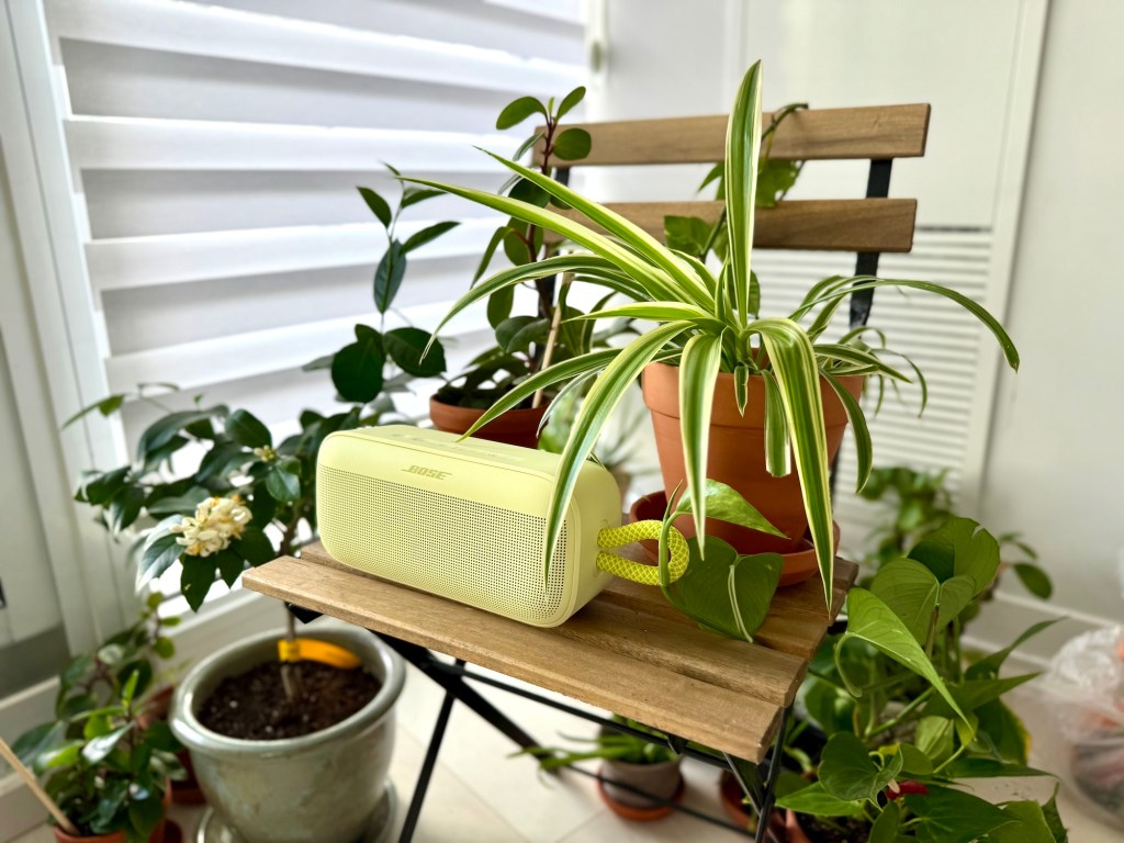 A small white speaker on a wooden table with potted plants