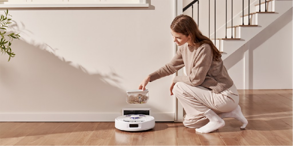 A woman kneeling on the floor with a robot vacuum