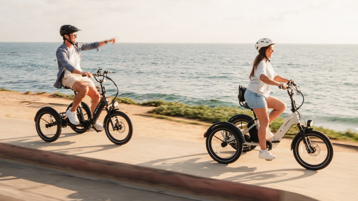 A man and woman riding bicycles on a sidewalk by the water