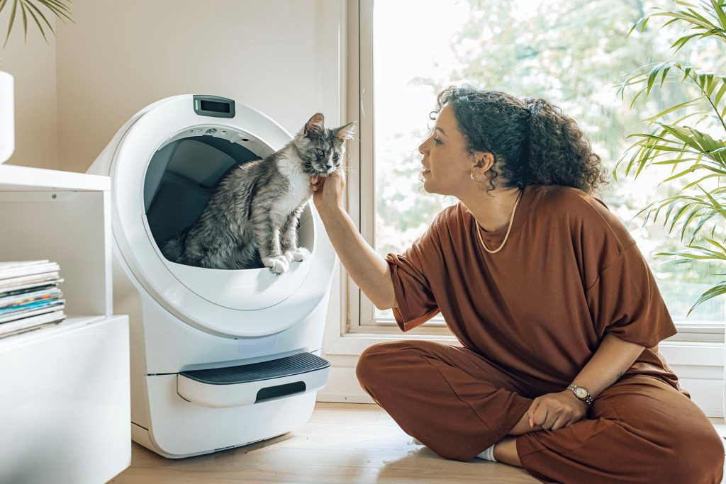 A woman sitting on the floor with a cat in a Whisker Litter-Robot 5