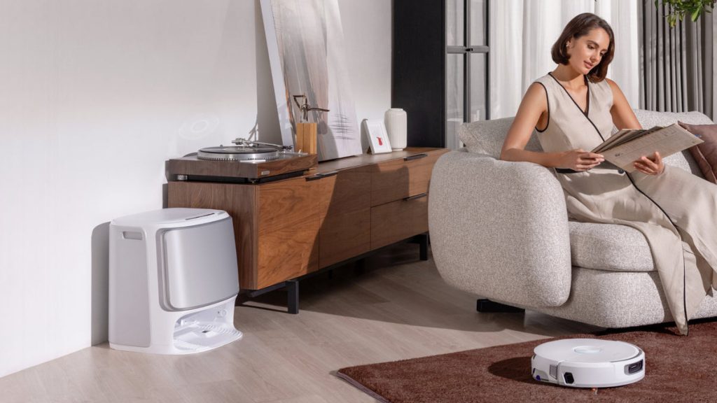 A woman sitting on a couch in front of a robot vacuum cleaner