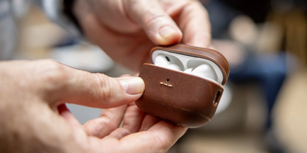 A person holding a brown case with white earbuds