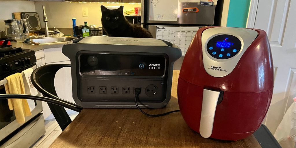 A cat sitting on a table next to an air fryer